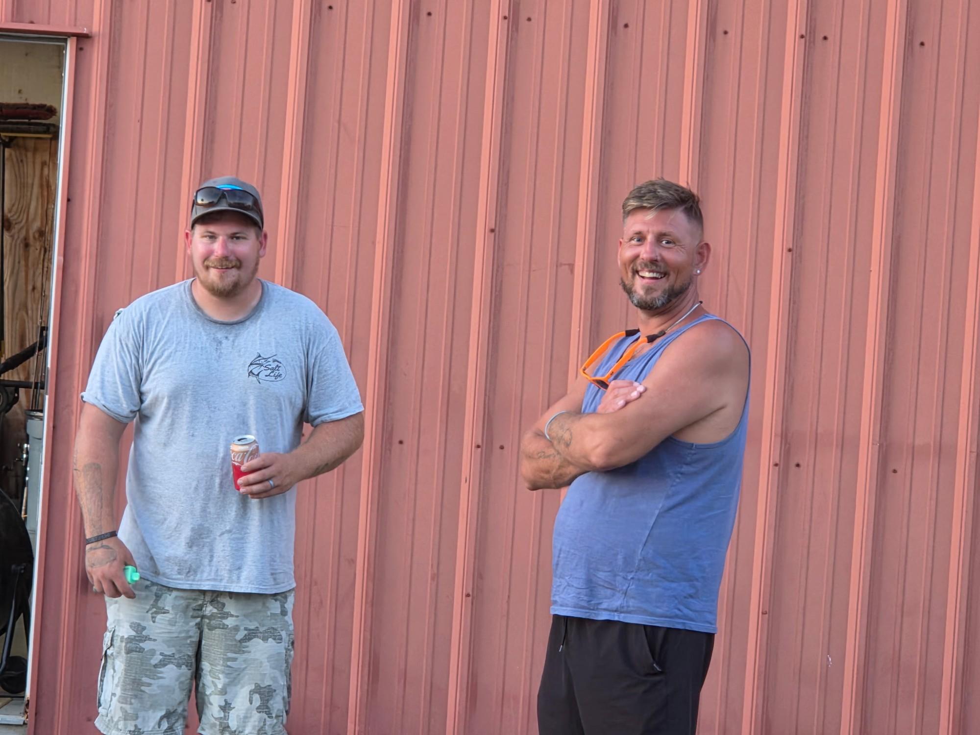 Two men smiling in front of a red metal building.